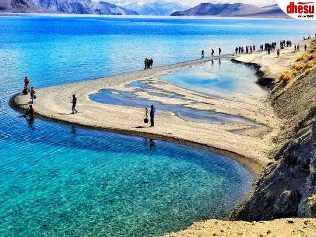 Walkers crossing a sandbar at a high-altitude mountain lake
