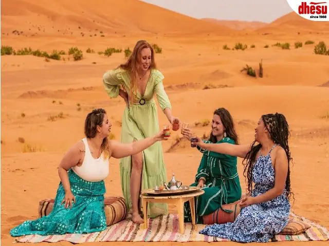 A group of travellers sharing tea around a table set up in the desert