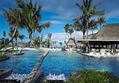 A resort pool ringed by palms and open-sided pavilions